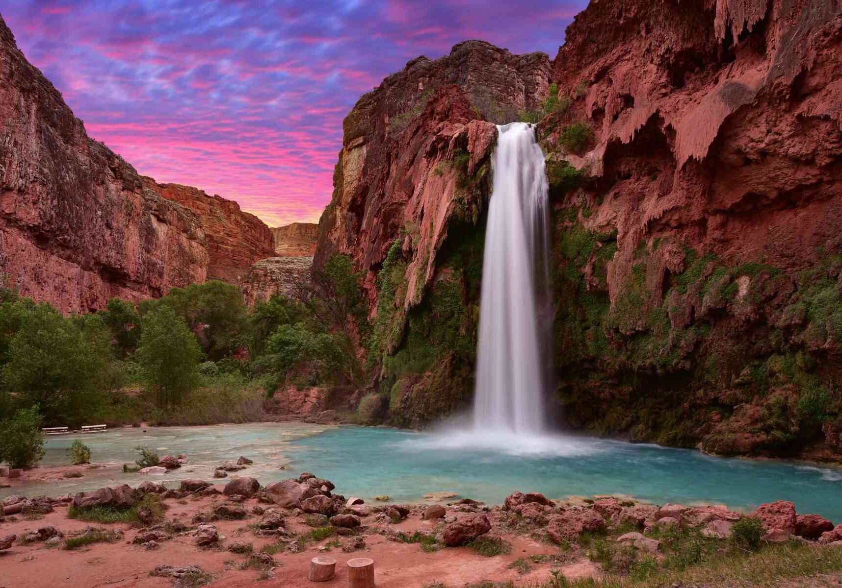 vibrant pink sky with red cliffs. and Havasu Falls waterfall flowing into a blue pool below.